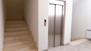 Un ascenseur moderne doté d’un panneau de commande, d’un escalier recouvert d’un tapis beige et d’un mur blanc.