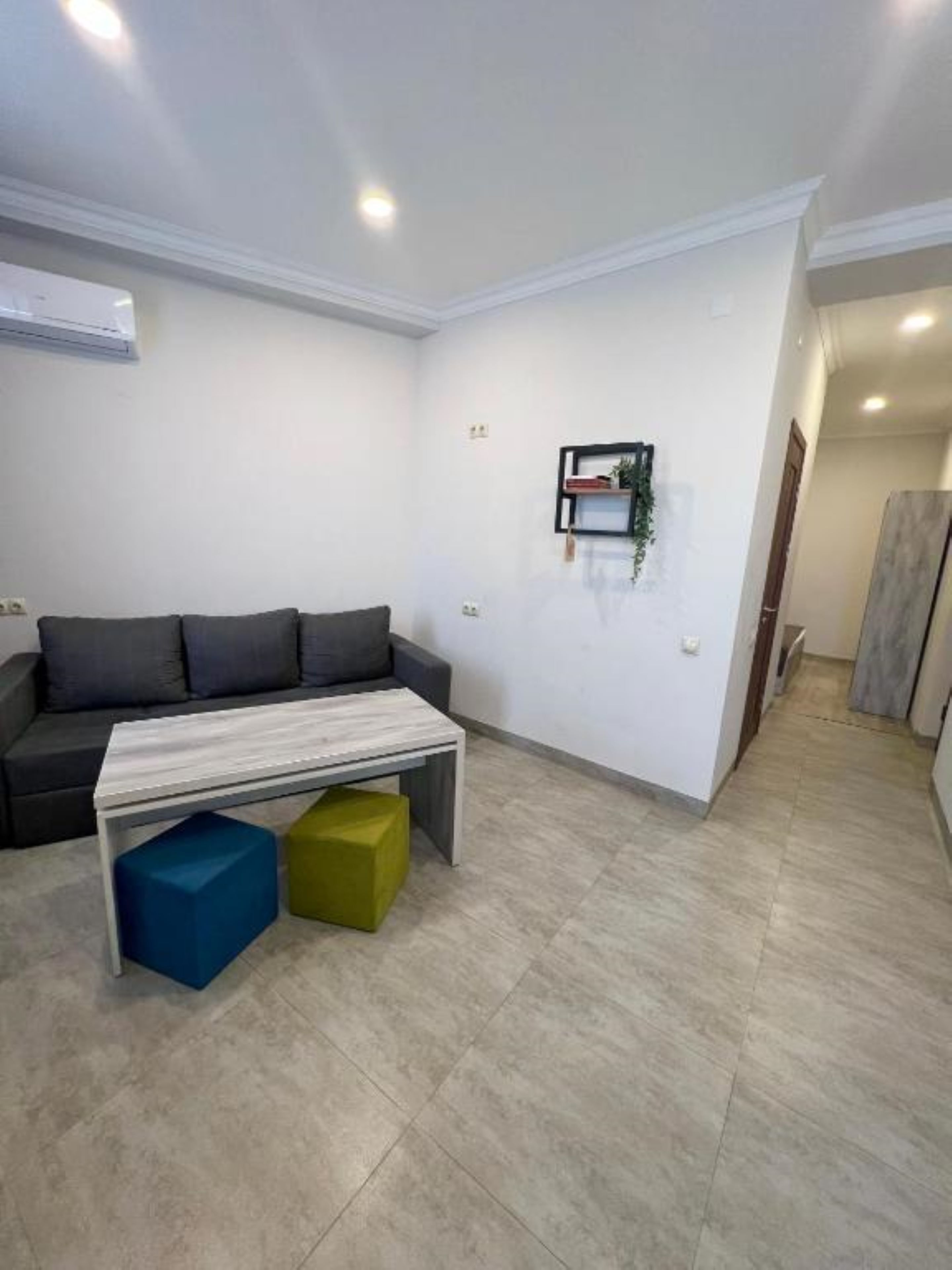 A modern living room with a grey sofa, a white coffee table, and colorful stools.