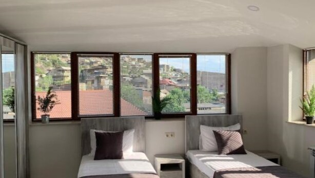 Une chambre moderne avec deux lits, de grandes fenêtres et une vue sur la ville.
