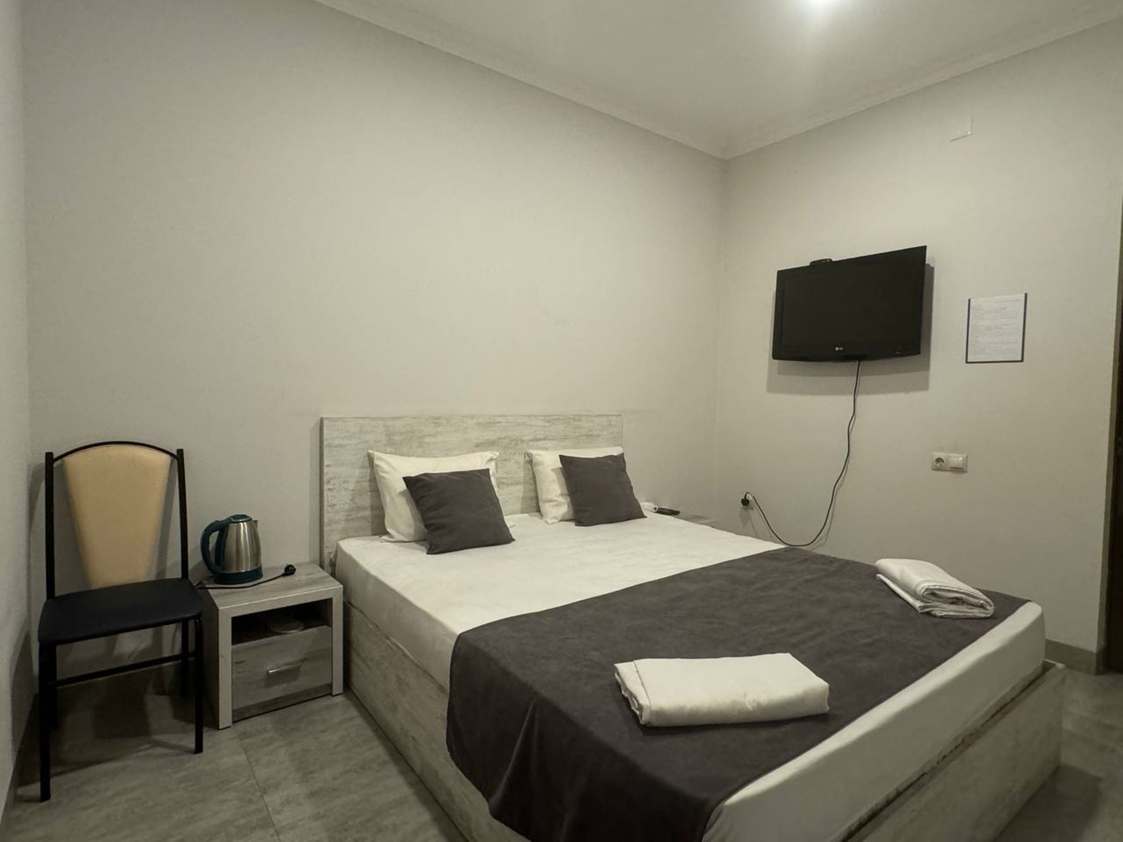 A hotel room with a bed, a chair, a nightstand, a TV, and a wall-mounted TV.