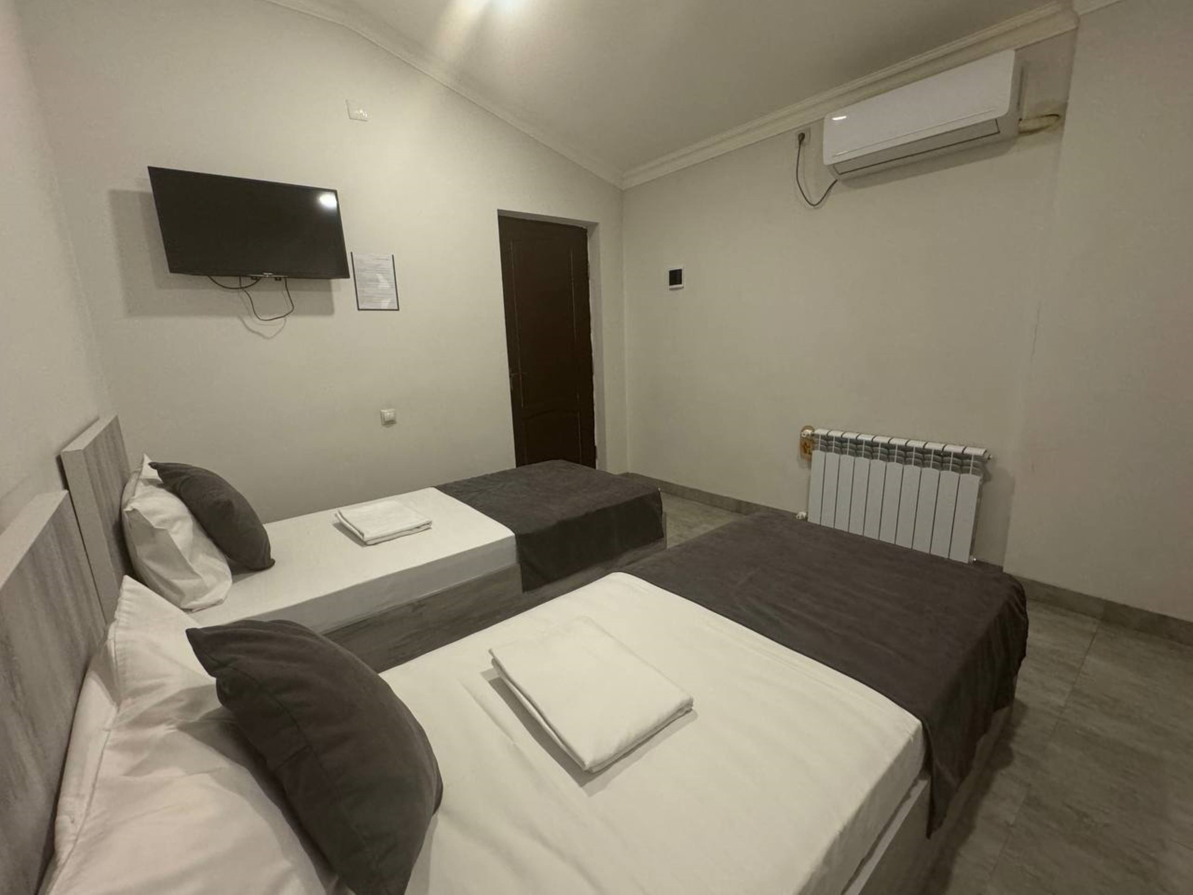 A hotel room with two single beds, a flat-screen TV, a door, and a radiator.