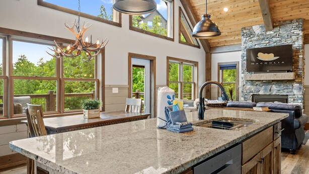 A spacious kitchen with a large island, a stone fireplace, and large windows offering views of the outdoors.