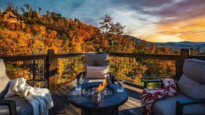 A deck with a fire pit, seating, and a view of autumn foliage and mountains.