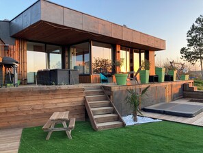 Une maison moderne dotée d’une terrasse en bois, d’un espace salon extérieur et d’un petit jardin.