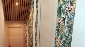 A hallway with wooden slats on the ceiling, a door at the end, and walls with tropical leaf patterns. - Beautiful architect-designed house in the Monts du Lyonnais region (Chabanière)
