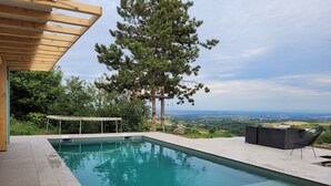 A rectangular swimming pool with a wooden pergola overhead, surrounded by a tiled deck. - Beautiful architect-designed house in the Monts du Lyonnais region (Chabanière)