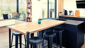 A modern kitchen with a wooden island, black bar stools, and a built-in bookshelf. - Beautiful architect-designed house in the Monts du Lyonnais region (Chabanière)