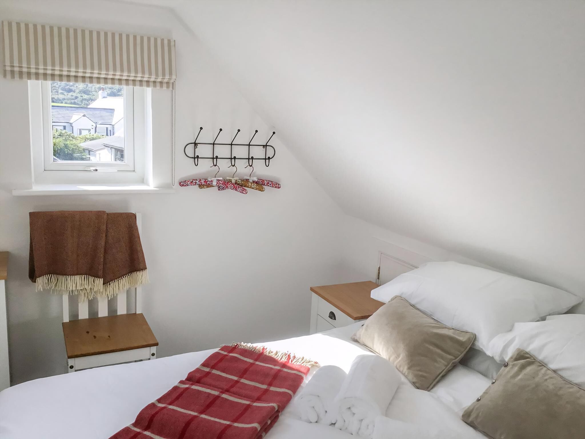 Una camera da letto con un letto, una finestra, un comodino, un attaccapanni e una panca.