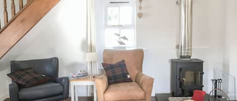 Ein gemütliches Wohnzimmer mit einer Holztreppe, einer Couch, einem Sessel, einem Tisch mit Büchern, einer Lampe, einem Kamin und einem Holzscheitkorb.