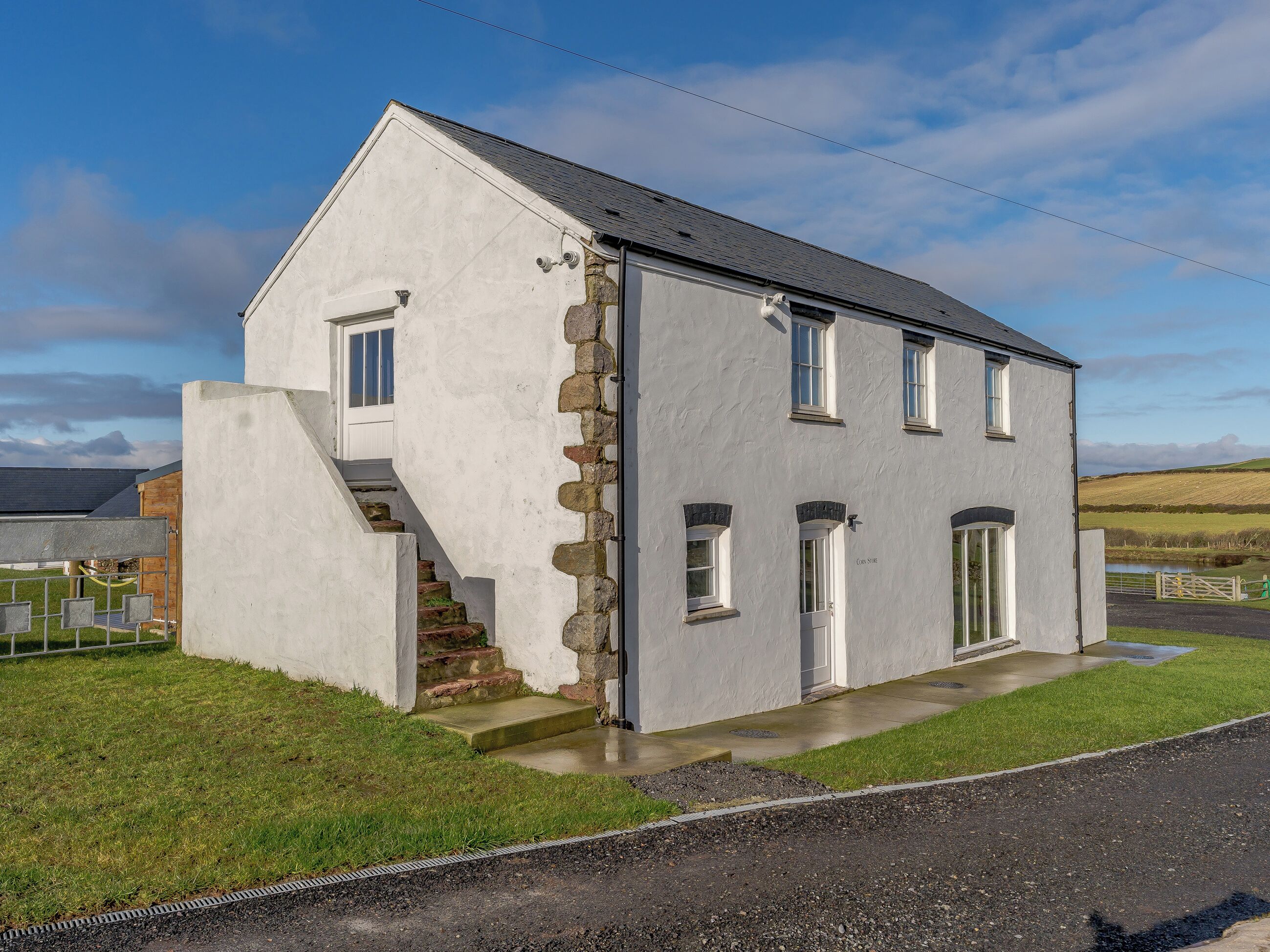 A two-story white building with a stone staircase, a small porch, and a view of the countryside.