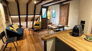 Une pièce chaleureuse avec un plancher en bois, un canapé bleu, un fauteuil jaune et une table à manger dressée pour deux personnes.