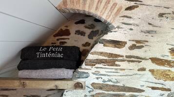 Ein Stapel Handtücher mit dem Schriftzug "Le Petit Inténiac" auf einem Regal vor einer strukturierten Wand.