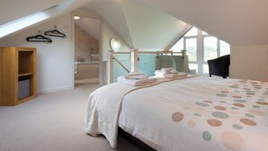 A bedroom with a sloped ceiling, a bed with a patterned bedspread, a wooden wardrobe, a bathroom with a bathtub, and a window providing natural light. - 3 bedroom accommodation in Kingswear (Kingswear)