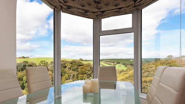 A glass-top table with four beige chairs in a room with large windows offering a view of a green landscape. - 3 bedroom accommodation in Kingswear (Kingswear)