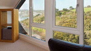 A room with a large window overlooking a scenic landscape, a wooden shelf, and a leather chair. - 3 bedroom accommodation in Kingswear (Kingswear)