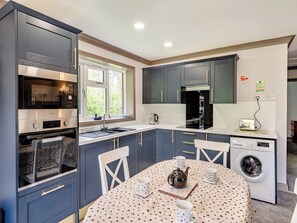 A compact kitchen with a built-in oven, microwave, and sink, a dining area with a table and chairs, and a washing machine.