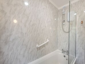 Ein Badezimmer mit einer gläsernen Duschkabine, einer weißen Badewanne und einer Marmorwand.