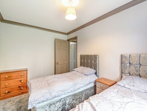 A bedroom with two beds, a wooden dresser, a nightstand, and a ceiling light fixture.