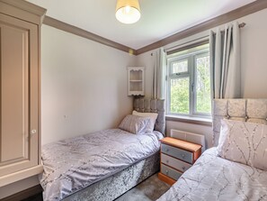 A bedroom with two beds, a wardrobe, a nightstand, a window with curtains, and a wall-mounted shelf. - A peaceful location for a relaxing break with excellent fishing to enjoy. (Marston)