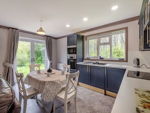 A modern kitchen with a dining area, featuring a table with chairs, a window with a view of greenery, and built-in appliances.
