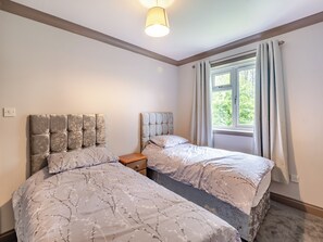 A bedroom with two beds, a window with curtains, and a ceiling light.