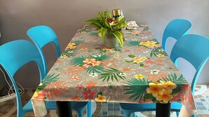 Una mesa de comedor con mantel floral, rodeada de sillas azules y una planta en maceta sobre la mesa.