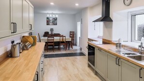 Une cuisine moderne avec des meubles de couleur bois clair, une hotte de cuisine en acier inoxydable et un coin repas comprenant une table et des chaises.