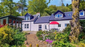 Une maison avec un jardin et un chemin qui mène à un patio agrémenté d’un parasol rouge.