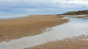 A beach with a lighthouse in the distance, sandy shore, and overcast sky.