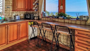 A kitchen with wooden cabinets, a built-in oven, a microwave, and a window with a view of the sea.