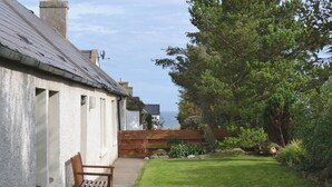 A house with a paved pathway leading to a bench, a wooden fence, and a grassy lawn.