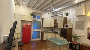 Una cocina compacta con armarios blancos, un refrigerador rojo y un comedor con mesa y sillas de vidrio.