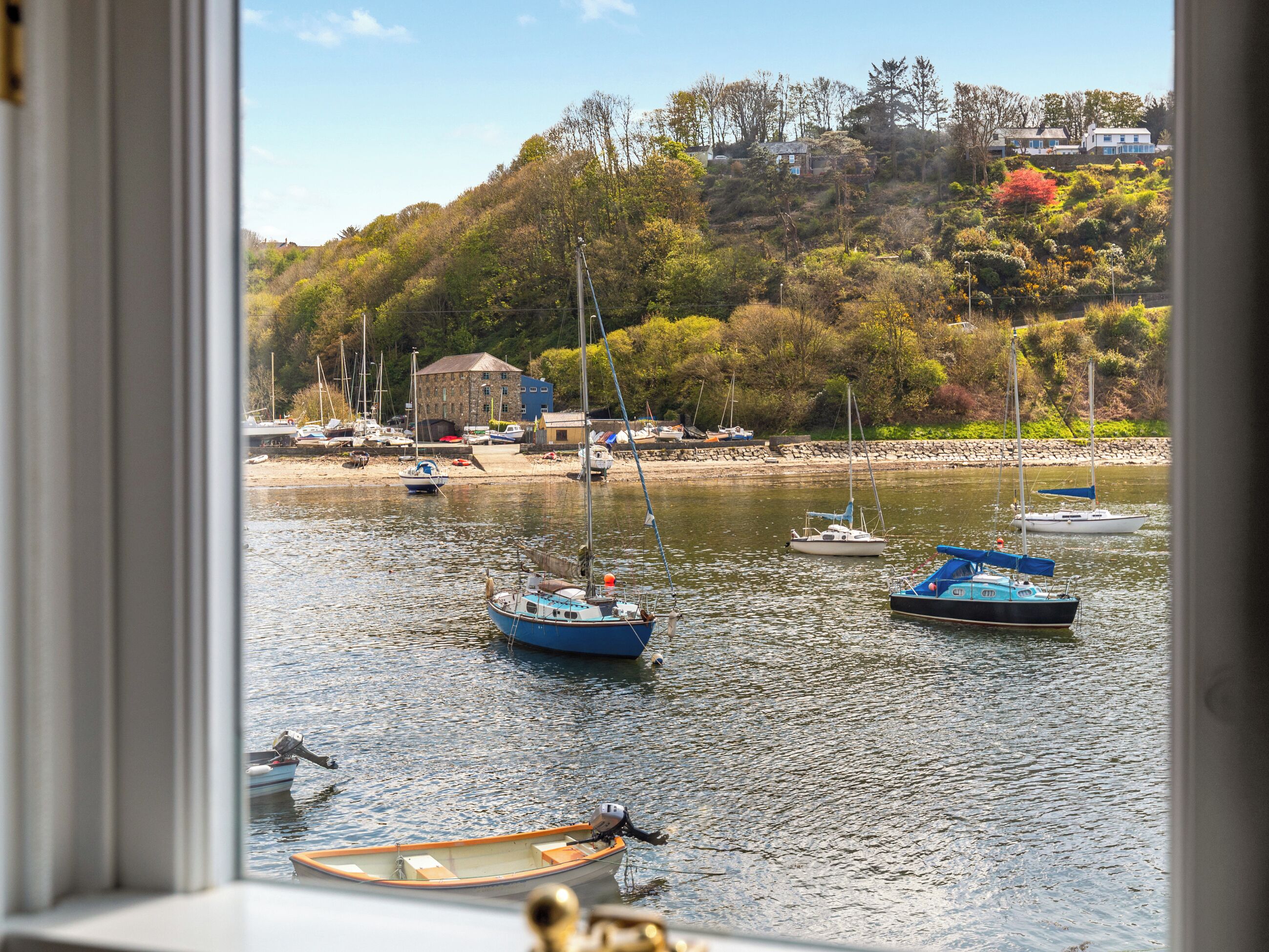A view of a harbor with boats, a building, and a hillside with trees.