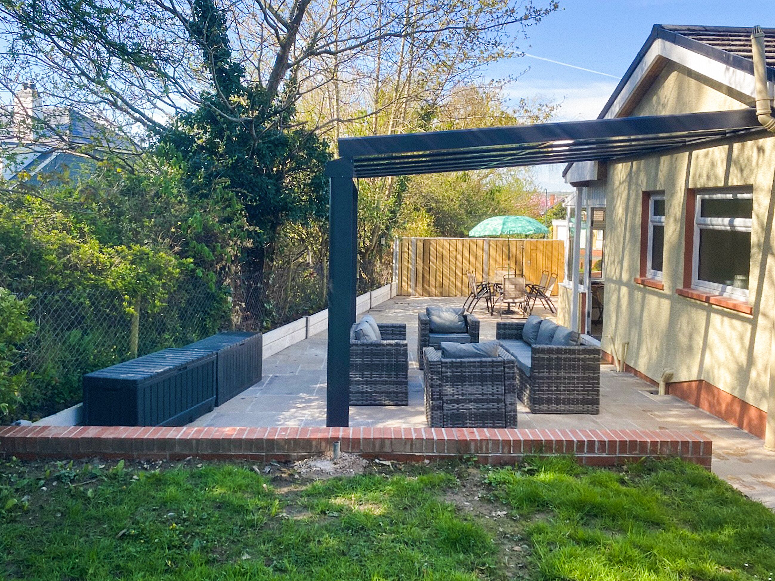 Um pátio com móveis de exterior, pérgola e cerca de madeira.