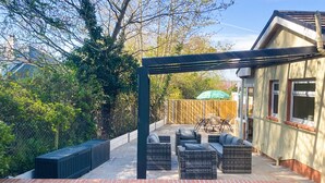 Un patio con mobiliario exterior, una pérgola y una valla de madera.