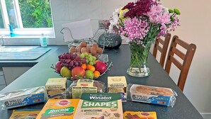 Una encimera de cocina con un frutero, un jarrón de flores y diversos alimentos, incluyendo pan y comida para perro.