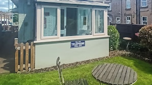 Il s’agit d’un petit bâtiment d’un seul étage, sur lequel on peut voir une enseigne indiquant qu’il propose des services de téléphonie. Il a un toit en pente, de grandes fenêtres et est entouré d’une clôture en bois et d’une zone herbeuse avec un banc.