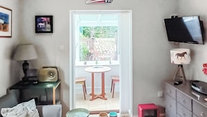 Un salon comprenant un canapé, une petite table, un téléviseur et une porte donnant sur un balcon équipé d’une table et de chaises.