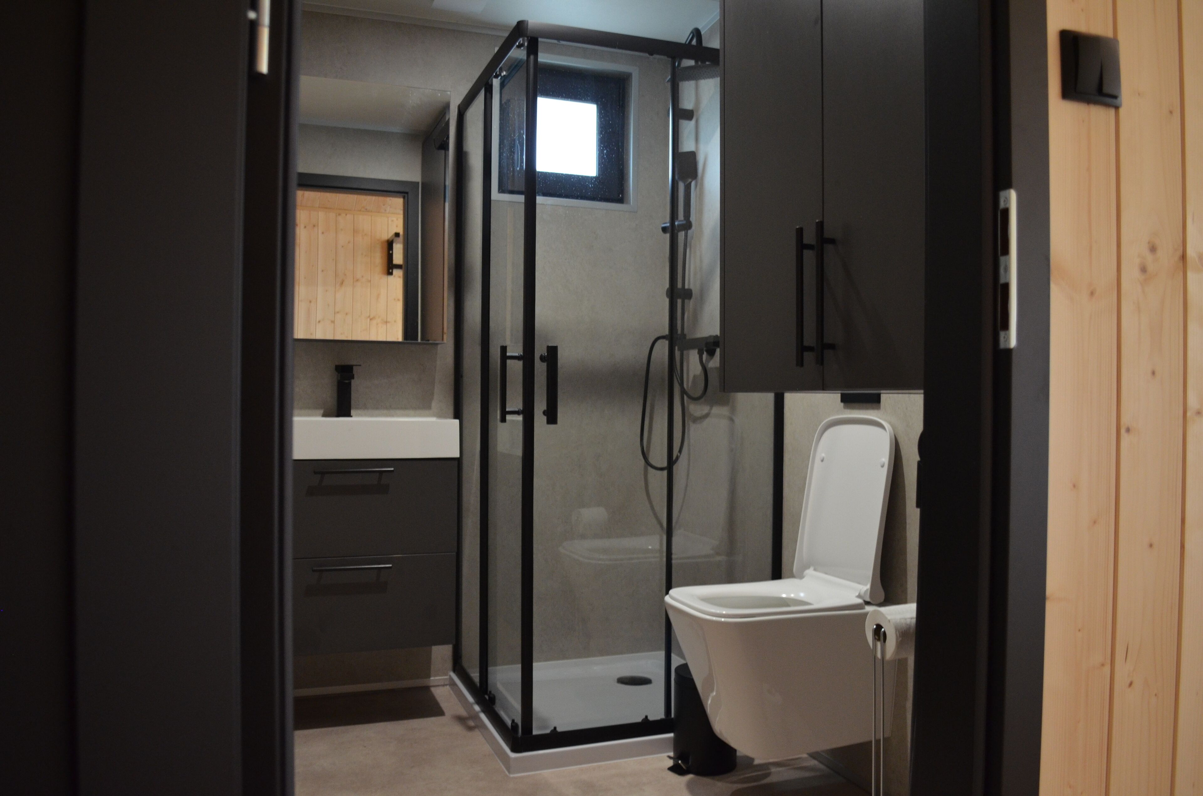 Une salle de bain moderne dotée d’une douche à parois de verre, de toilettes et d’un lavabo.