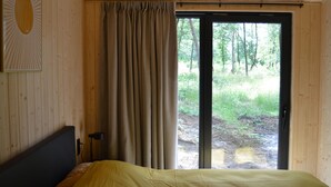 Una habitación con cama, cortina y puerta que da a un espacio exterior con árboles.