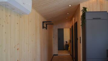 A narrow hallway with wooden walls and a ceiling, leading to a room with a refrigerator and a suitcase.