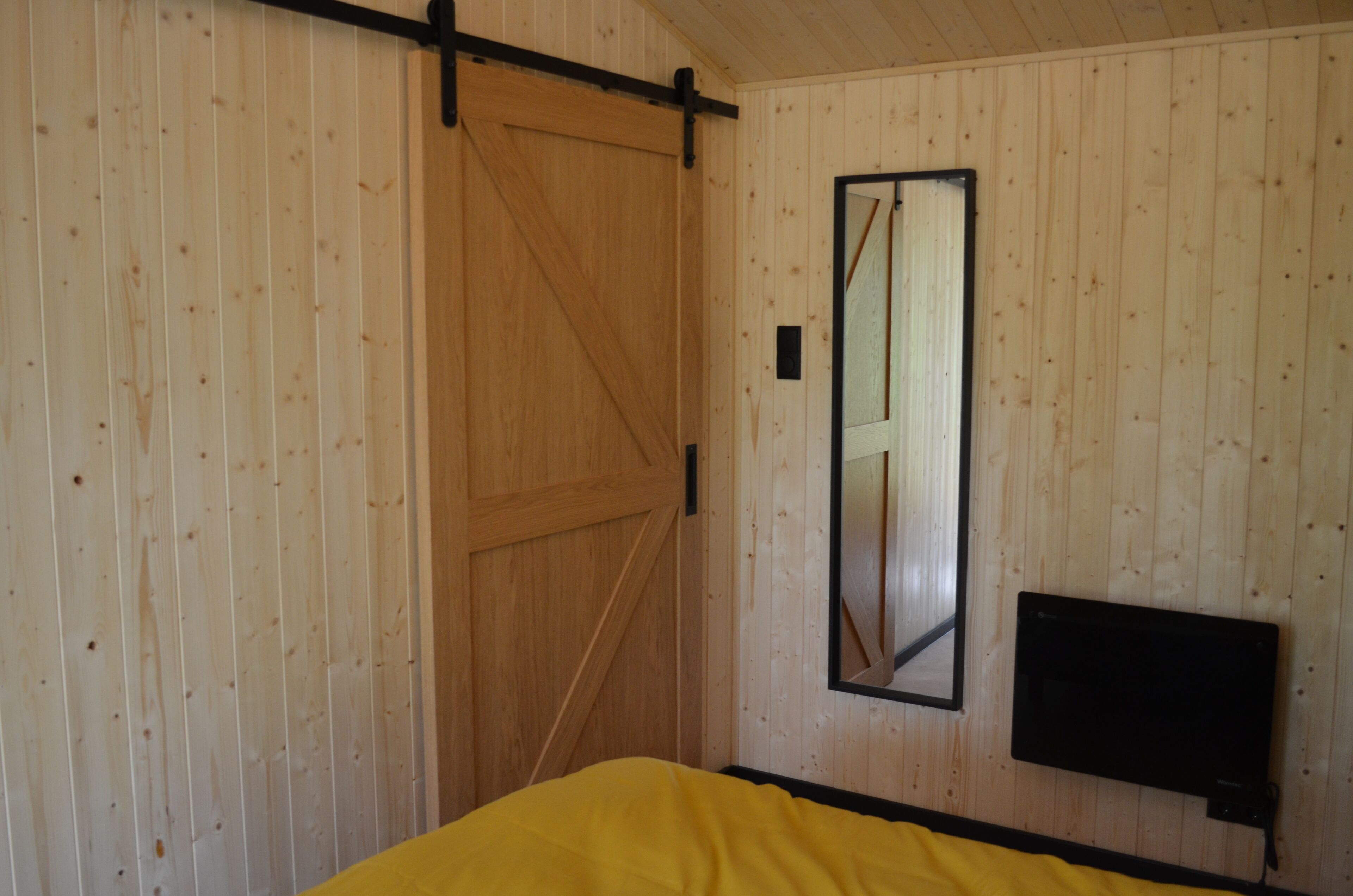 Een kamer met een houten schuifdeur, een spiegel en een flatscreen televisie aan de muur.