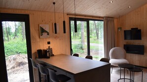 Una cocina moderna con una isla central, taburetes de bar, un televisor y un amplio ventanal con vistas al exterior.