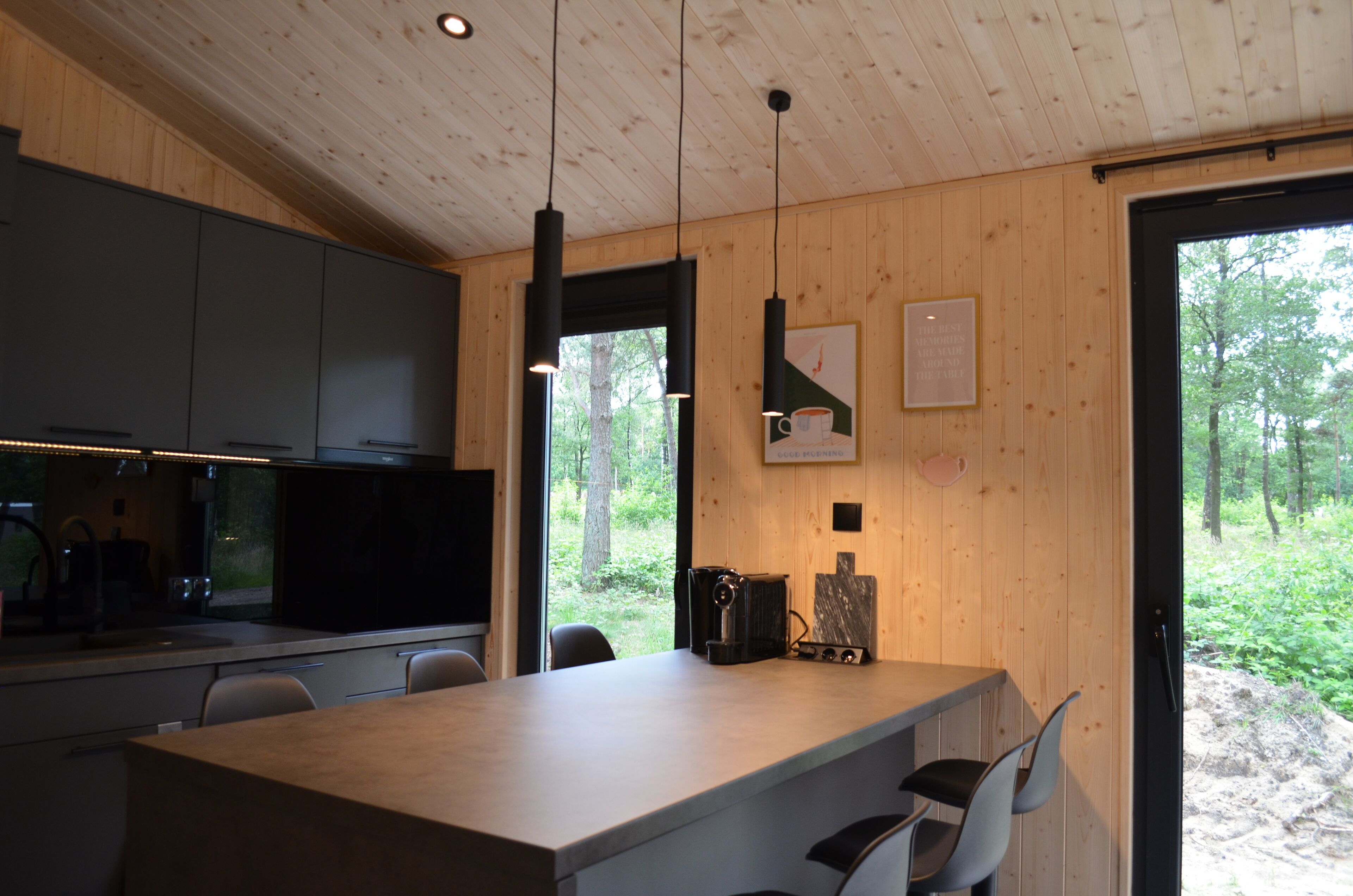 Una cucina moderna con mobili scuri, soffitto in legno e un'ampia finestra vista foresta.