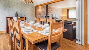 A dining room with a wooden table set for six, surrounded by wooden chairs with black cushions.