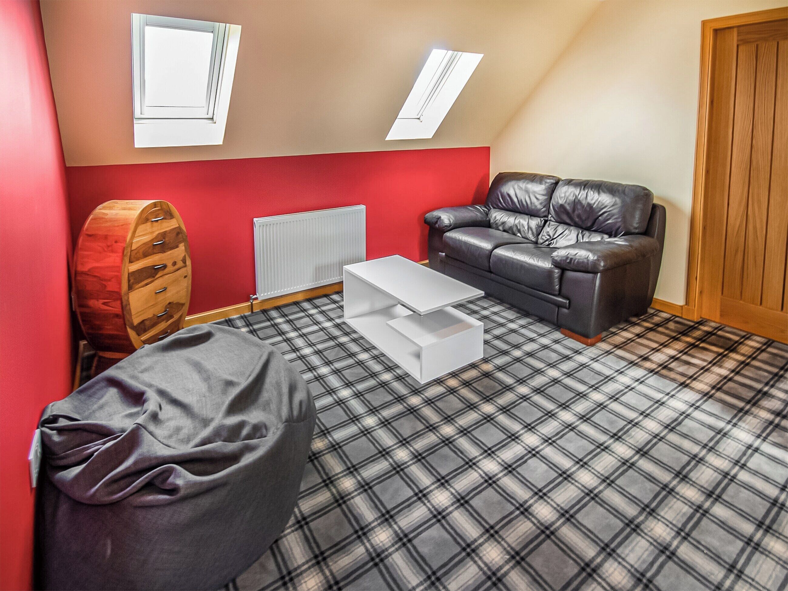 Une pièce avec un mur rouge, un canapé en cuir noir, une table basse blanche, un sol à motifs écossais, un tonneau en bois et un radiateur.