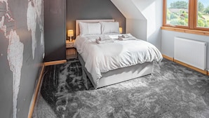 A bedroom with a bed, a nightstand, a lamp, a window, and a radiator.