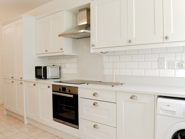 Une cuisine moderne avec des meubles blancs, un four encastré, un four à micro-ondes et un lave-vaisselle.