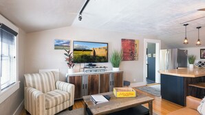A modern living room with a striped armchair, a wooden coffee table, and a television mounted on the wall. - The Loft on Humphreys:  A Charming 2 BR Apartment in Downtown Flagstaff with A/C (Flagstaff)