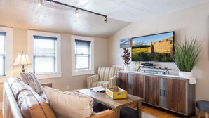 A living room with a sofa, armchairs, a coffee table, a TV, and a cabinet. - The Loft on Humphreys:  A Charming 2 BR Apartment in Downtown Flagstaff with A/C (Flagstaff)